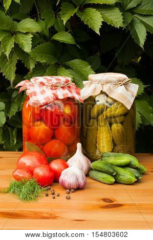 Canned And Fresh Vegetables. Canned Tomatoes And Pickled Cucumbers In Glass Jars On Wooden Table Outdoor. Homemade Canned Vegetables.