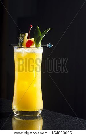 Mango cocktail decorate with pineapple and cherry against black background has reflect on the ground
