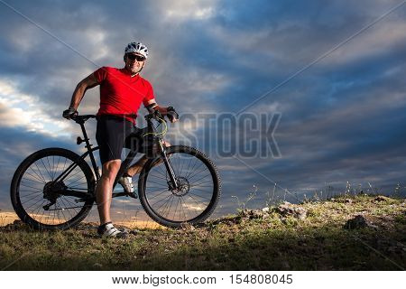 Sportive man with bicycle against sunset and cloudy sky
