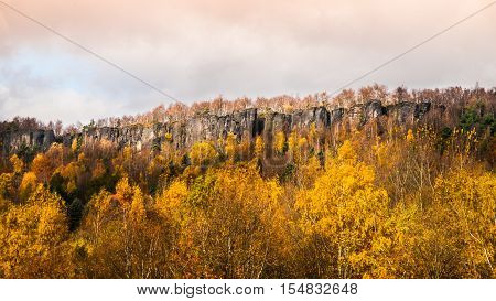 Panoramic view of sandstone rock formation in the middle of colorful autumn forest. Dramatic evening view. Tisa Rocks, aka Tiske Walls, Czech-Saxon Switzerland, Czech Republic