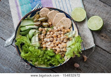 healthy salad in a bowl. olives, lime, chickpeas, paprika tofu,  cucumber  and tahini. more greens every day