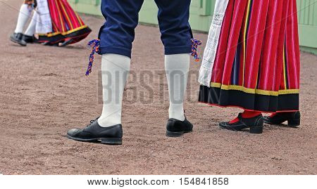 Legs of man and woman who are dressed in traditional Estonian clothing. They look at dancing couple and are going to dance too.