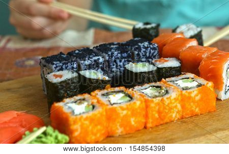 japanese sushi roll set in row on wooden kitchen board with sticks vasabi mustard and ginger close up photo