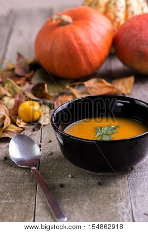 Autumn pumpkin soup on natural wooden table with colored leaves behind.