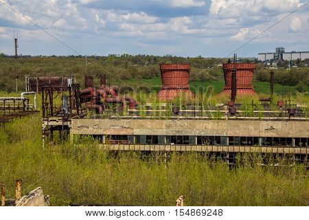 Abandoned factory of synthetic rubber overgrown by trees, ruins of buildings and cooling towers