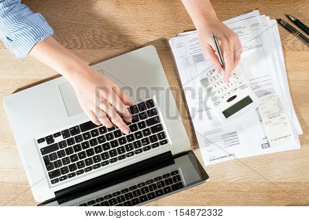 Doing Accounts At Desk With Pen, Calculator And Laptop
