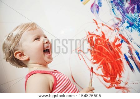 Portrait of cute adorable white Caucasian little boy girl playing and painting with paints on wall in bathroom having fun lifestyle childhood concept