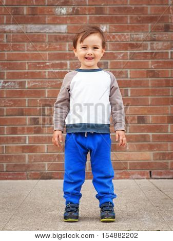 Portrait of a cute adorable little boy toddler two or three years old standing by brick wall and smiling laughing posing outside in the street