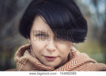 Closeup portrait of middle aged white caucasian dark haired brunette woman with short bob hairstyle with green eyes with yellow orange woolen scarf on her neck looking directly in camera outside in autumn fall park stylish sexy fashion concept