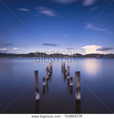 Wooden pier or jetty remains on blue lake sunset and sky reflection water. Long exposure Versilia Massaciuccoli Tuscany Italy.