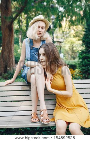 Portrait of two white Caucasian unformal young girls hipster students teenagers friends outside in park on summer day sitting on bench together best friends forever