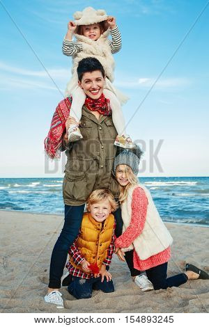 Group portrait of white Caucasian family mother with three children kids hugging smiling laughing on ocean sea beach on sunset outdoors looking in camera happy lifestyle childhood concept