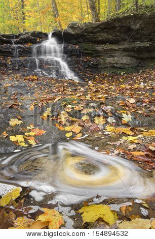 A swirl in a stream surrounded by fallen autumn leaves is backed by a small cascading waterfall in Indiana's Lieber State Recreation Area.
