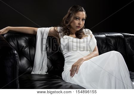 Bridal modeling modern fashion trend of simple but elegant thin wedding dress in retro or art deco style. Bride on couch with shoulder scarf and bridal gown.