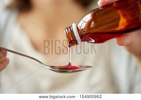 healthcare, people and medicine concept - woman pouring medication or antipyretic syrup from bottle to spoon
