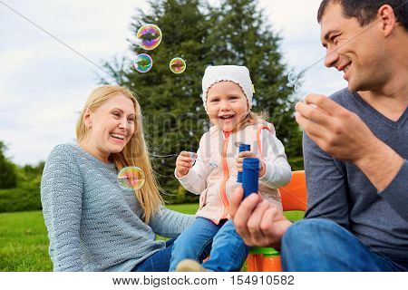 Family playing with bubbles outdoors. Mother dad and child in the park.