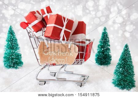 Label With German Text Geschenk Ideen Means Gift Ideas. Trollye With Christmas Gifts Or Presents. Snowy Scenery With Snow And Trees. Sparkling Bokeh Effect.