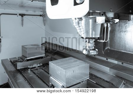 The face milling tool with the raw material work piece on the CNC milling machine in the silver tone effect.
