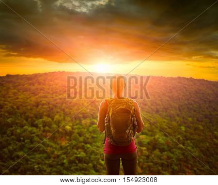 Travelling woman with backpack looking green mountains and inspiring sunset with dramatic clouds. Tourist girl traveling along Asia active lifestyle concept