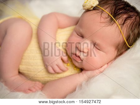 lovely newborn baby in yellow romper and headband sleeping with legs crossed