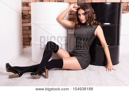 Beautiful slender brunette in a short slinky dress and stockings sitting on the floor. Sensual young woman in fashionable short dress and stockings.