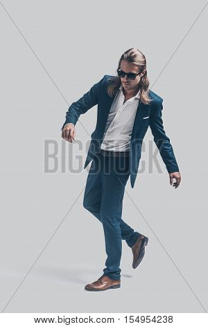 Style in motion. Full length of handsome young man in full suit posing against grey background