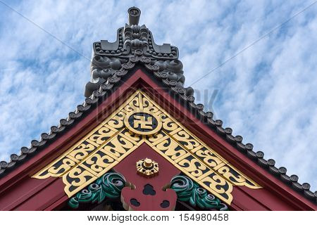 Tokyo Japan - September 26 2016: Closeup of highly gold vermilion and gray decorated top of Honzo hall at Senso-ji Buddhist Temple. Against blue cloudy sky.