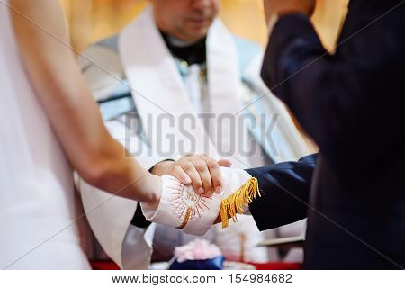 Bride And Groom's Hands Wrapped In Priest's Cassock