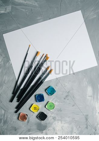 Painting Brusches, White Paper And Watercolors On Gray Concrete Background. Flat Lay, Top View