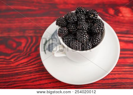 Black Berries In A White Cup On A Red Wooden Background