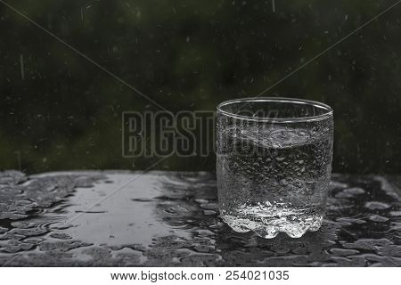 Conceptual Image With A Glass Abandoned In The Rain, To Be Filled With Water, Surrounded By Droplets