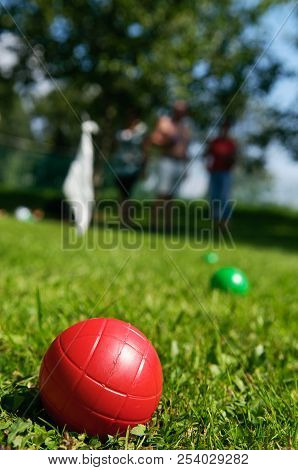 Closeup Of Red Boccia Ball Lying In Grass And People Playing In Background