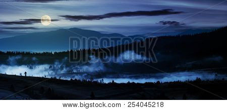Panorama Of Countryside At Night In Full Moon Light. Beautiful Landscape In Mountains With Fog Risin