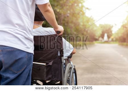 Caretaker And Daughter Spending Time Outdoor With Patient In Wheelchair.