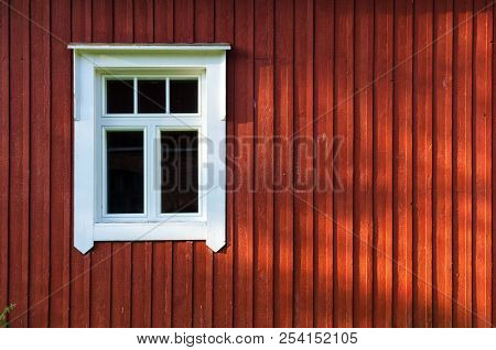 Fragment Of The Wall Of A Wooden Scandinavian House With A Window. A Wall Of Brown Is Lit By The Sun