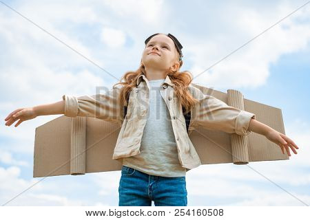Low Angle View Of Child With Paper Plane Wings And Protective Eyeglasses With Outstretched Arms Agai