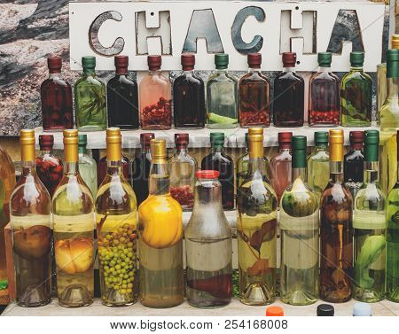 Traditional Georgian Alcohol Drink Chacha In Bottles With Different Fruits And Herbs Selling At Mark