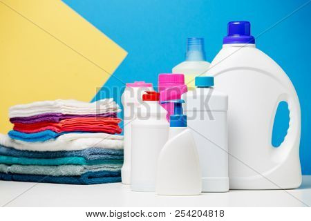 Photo of different bottles of cleaning products and colored towels on table isolated on blue, yellow background