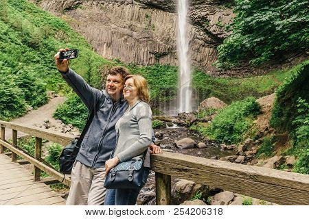 Couple Taking Selfie In Front Of Latourell Falls Waterfall Along The Columbia River Gorge, Oregon, U