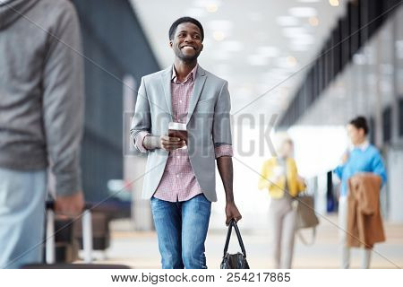 Cheerful African-American man standing with passport in hall of airport