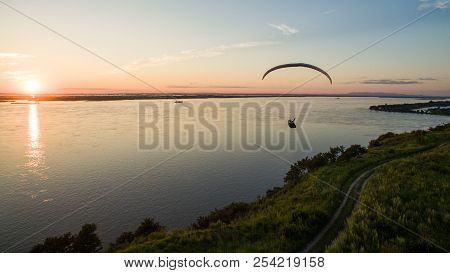 Silhouette Flying Paramotor Over River And Sunset Sky