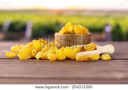 Lot Of Whole Dry Golden Raisins Sultana Variety Scoop With Wooden Bowl With Vineyard In Background