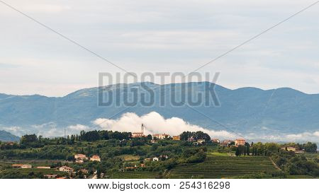 Village Of Steverjan, San Floriano Del Collio, Italy With Church In Front Of White Low White Cloud, 