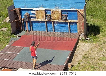 Adult Man Trains To Throw Knives In A Wooden Target On A Sunny Summer Day In The Park
