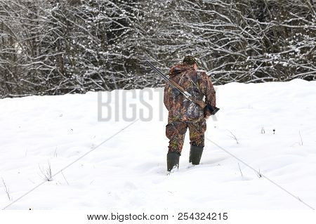 Hunter In Winter Camouflage With Shotgun In The Forest