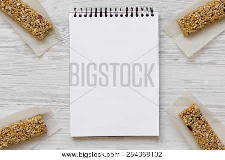 Granola Bars With Blank Notepad On White Wooden Table, Overhead View.