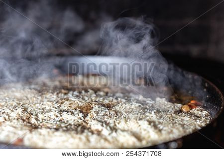 Cooking Rice For Pilaw Or Paella In Iron Cauldron Over Open Fire. Smoke And Steam. Tasty Food Prepar