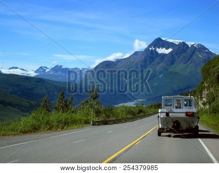 Traveler Hauls His Boat Through The Alaskan Wilderness.  Highway Leads Toward A Huge Glacier Covered