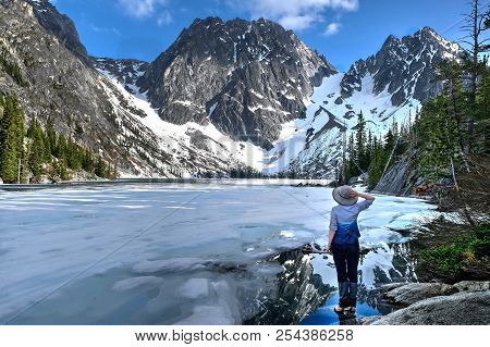 Hiking In Washington State. Woman Stading By Beautiful Lake Covered With Ice And Reflections In Wate