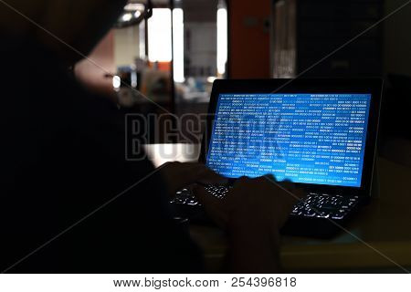 Computer Hacker Silhouette Typing On Computer In A Dark Room. Working On Blue Binary Code Technology